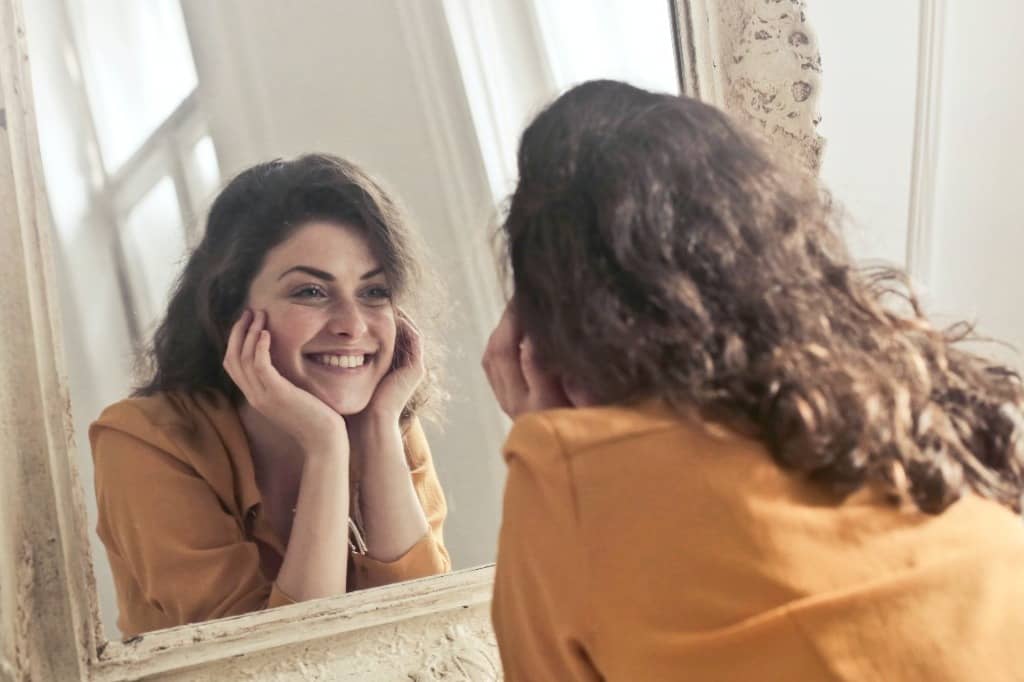 mujer sonriendo ante un espejo por estetica dental en quito